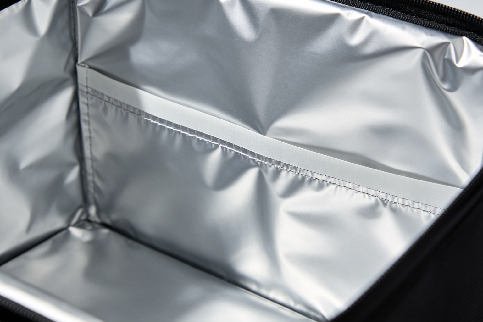 Close-up detail of food-grade PEVA aluminum foil lining inside a cooler bag, showing the reflective foil surface, sealed seams, and zipper closure with no gaps for cold air escape