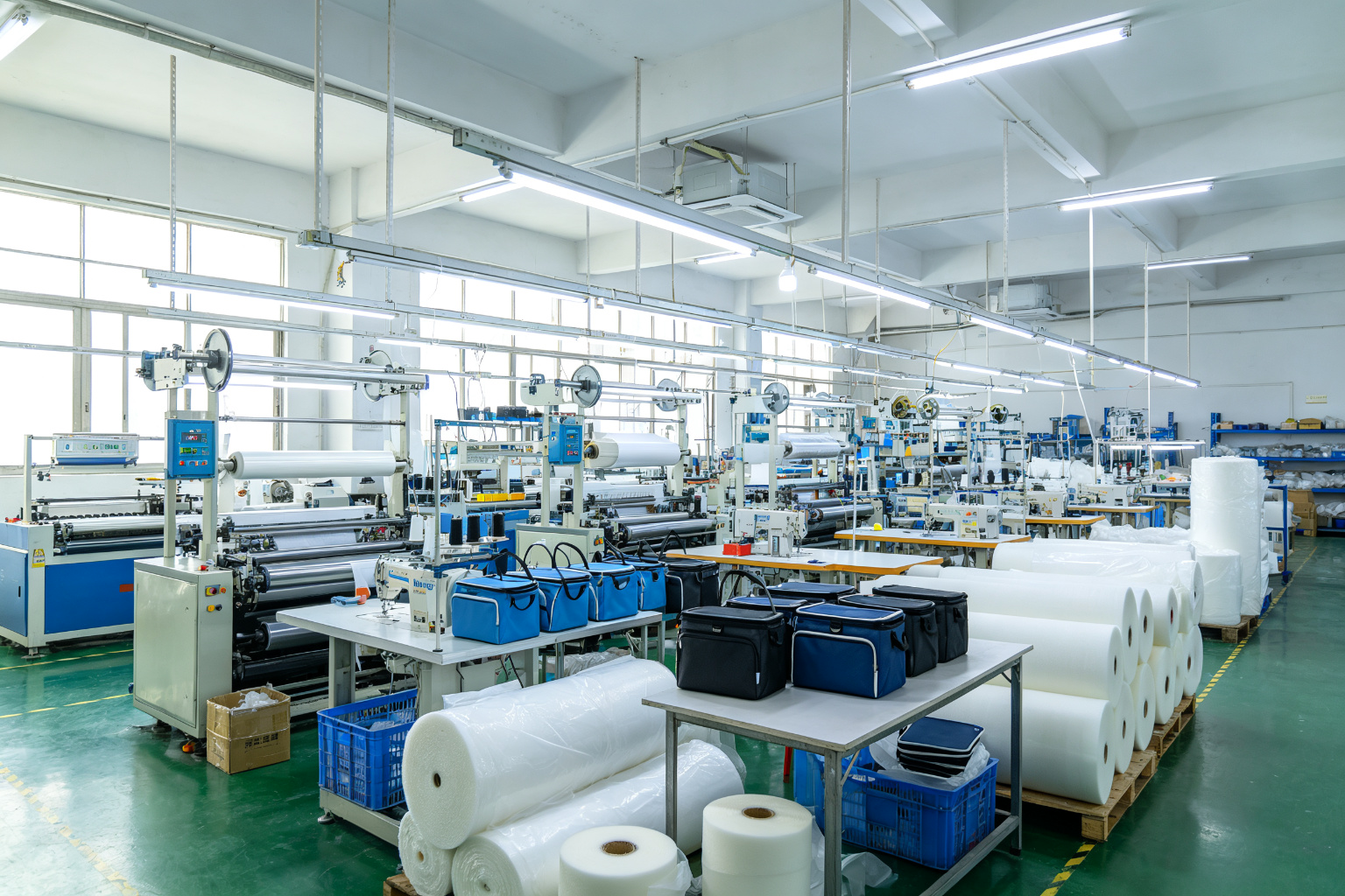 Wide angle view of insulated cooler bag manufacturing factory in Dongguan showing lamination machines, sewing production lines, and material storage
