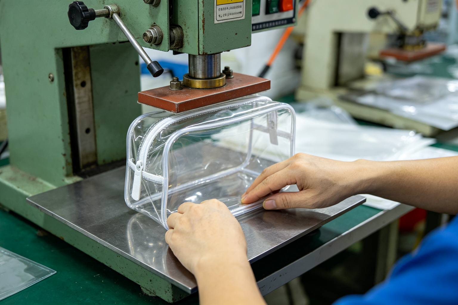 Factory worker operating a high frequency heat welding machine to seal seams of a transparent TPU cosmetic bag in a Dongguan bag workshop