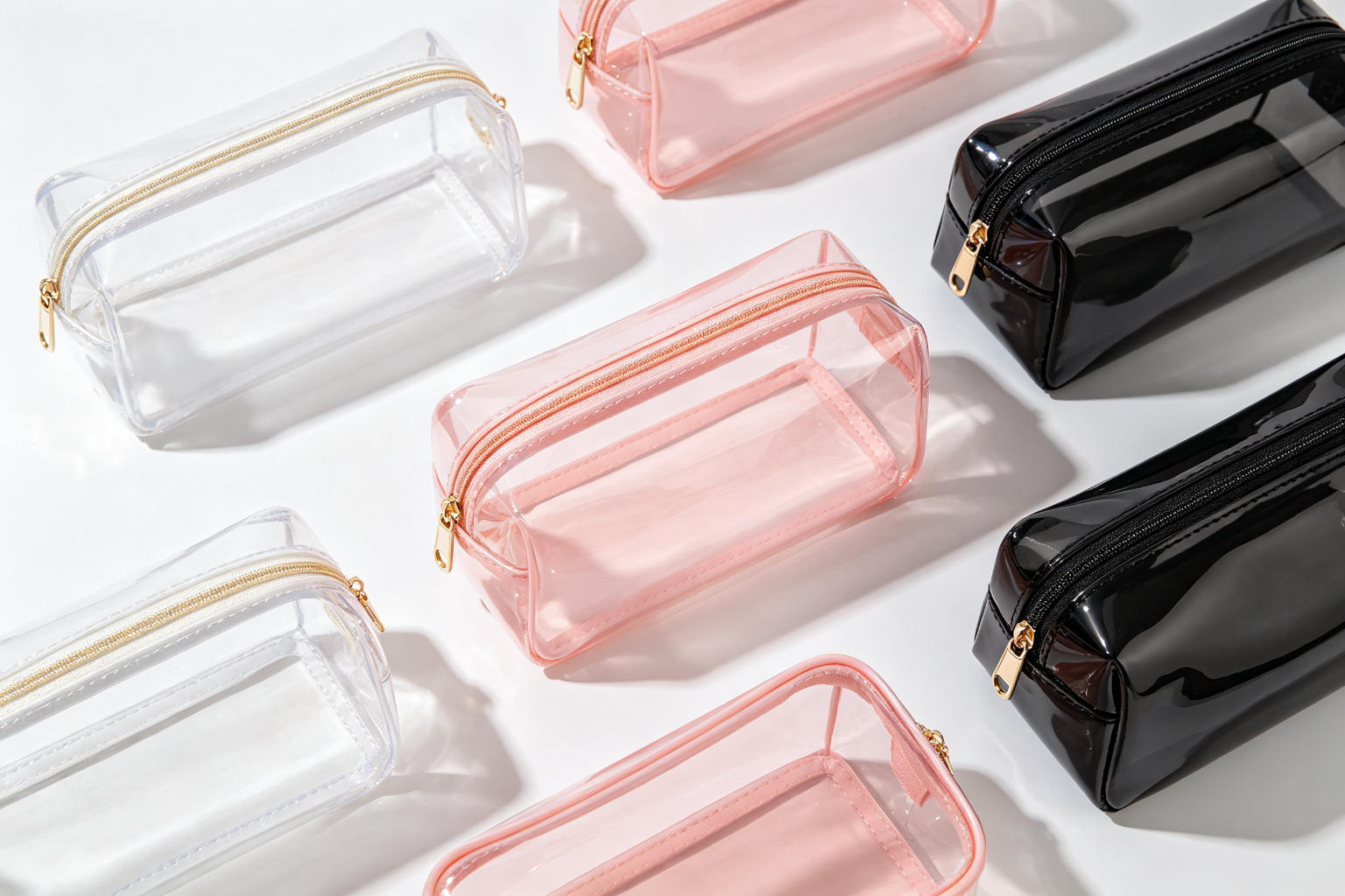 Flat lay of multiple transparent TPU cosmetic bags in clear, pink, and black colors arranged on white surface showing finished product variety