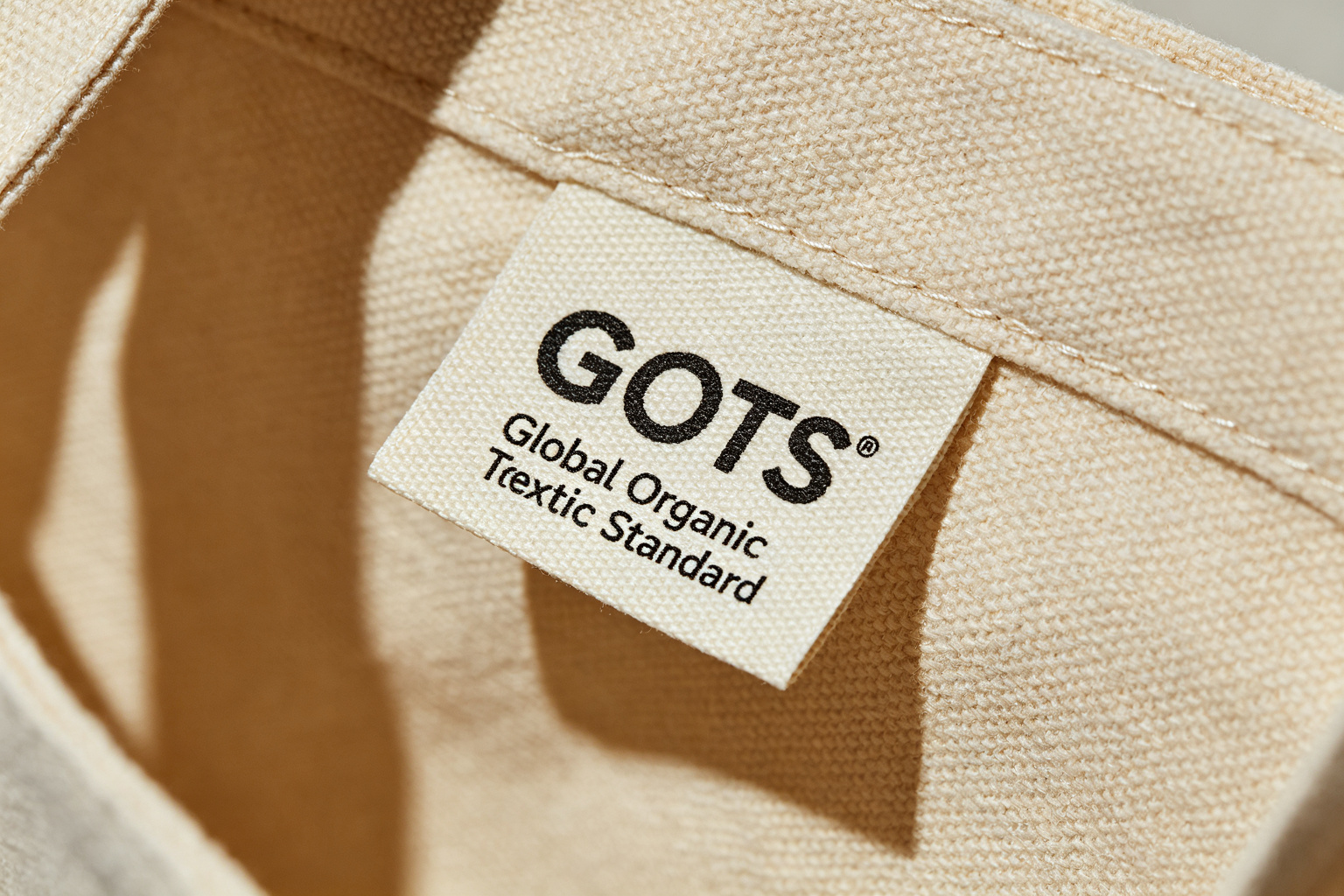 Close-up of GOTS Global Organic Textile Standard certification woven label sewn inside a natural organic cotton canvas tote bag showing label texture and canvas weave