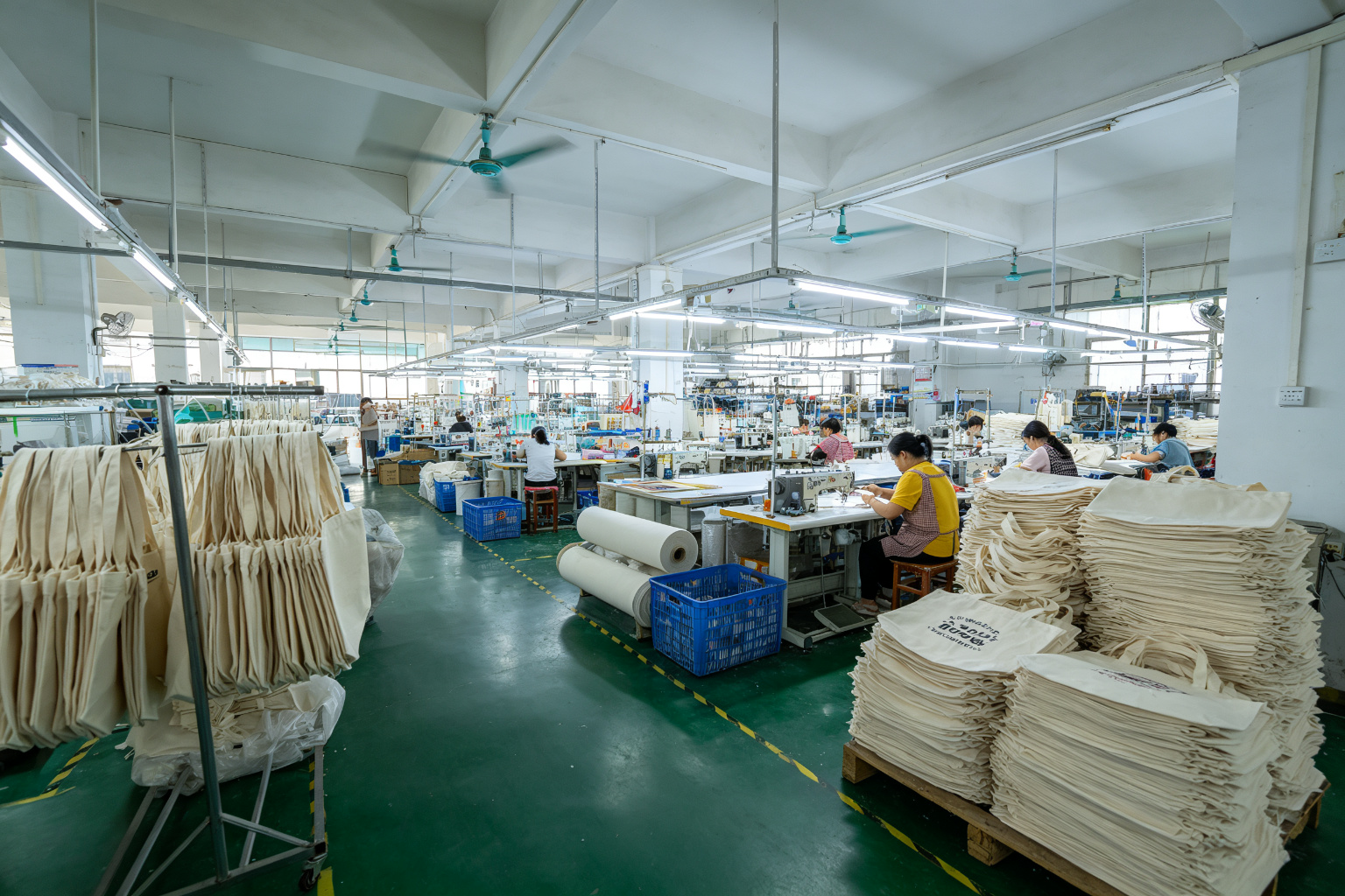 Wide angle view of canvas tote bag manufacturing workshop in Dongguan showing screen printing area with drying racks and sewing production lines