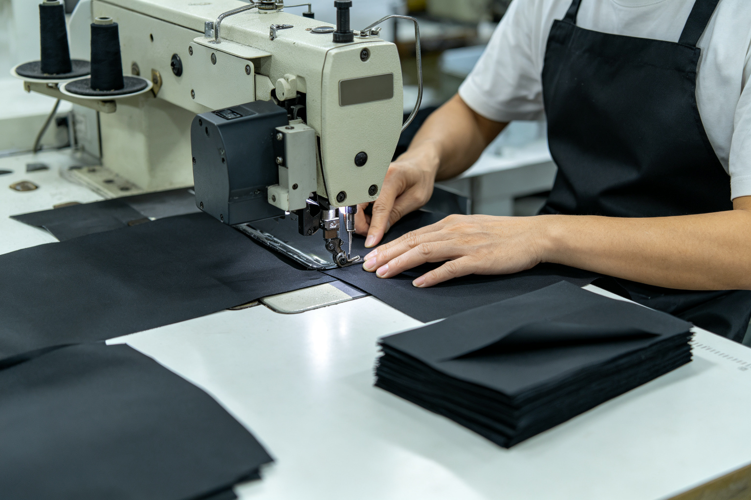 Factory worker cutting black nylon fabric panels with a cutting machine for a small batch waist bag order