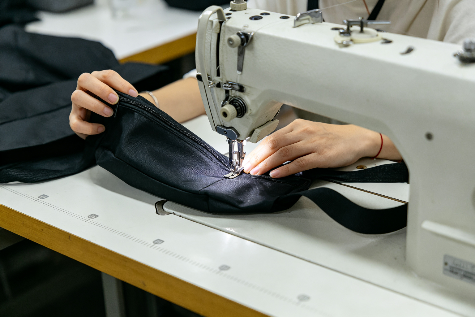 Worker sewing a black waist bag on an industrial sewing machine in a clean bag factory