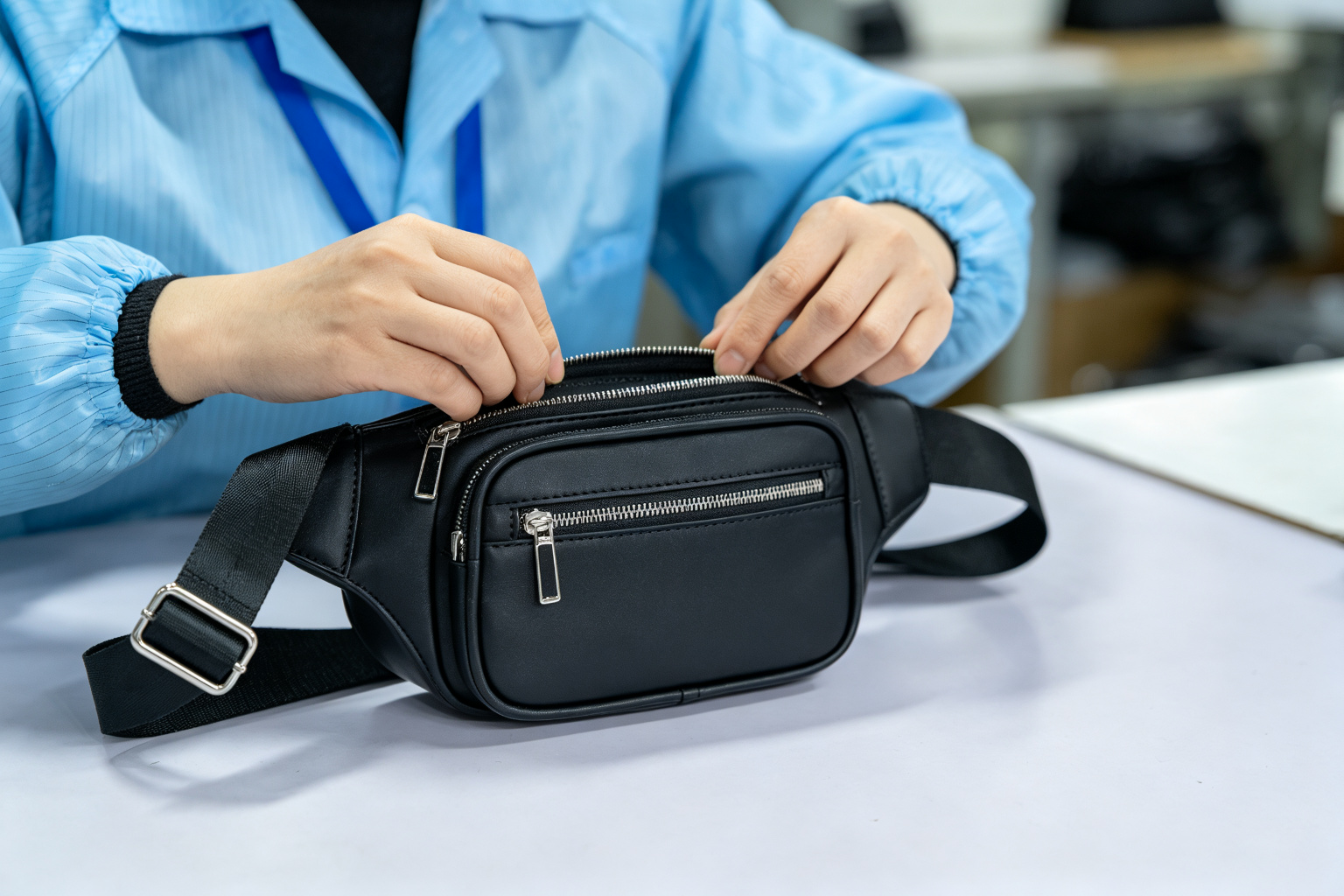 QC inspector examining a finished black waist bag at a quality control station, checking zipper and strap buckle