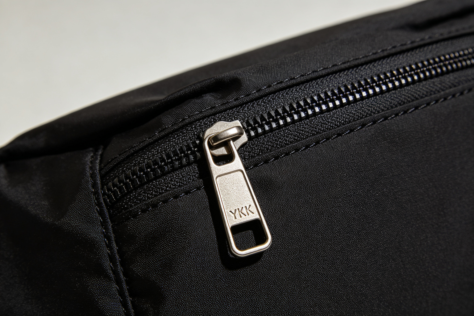 Close-up of a YKK zipper on a black nylon waist bag showing metal slider and stitch detail