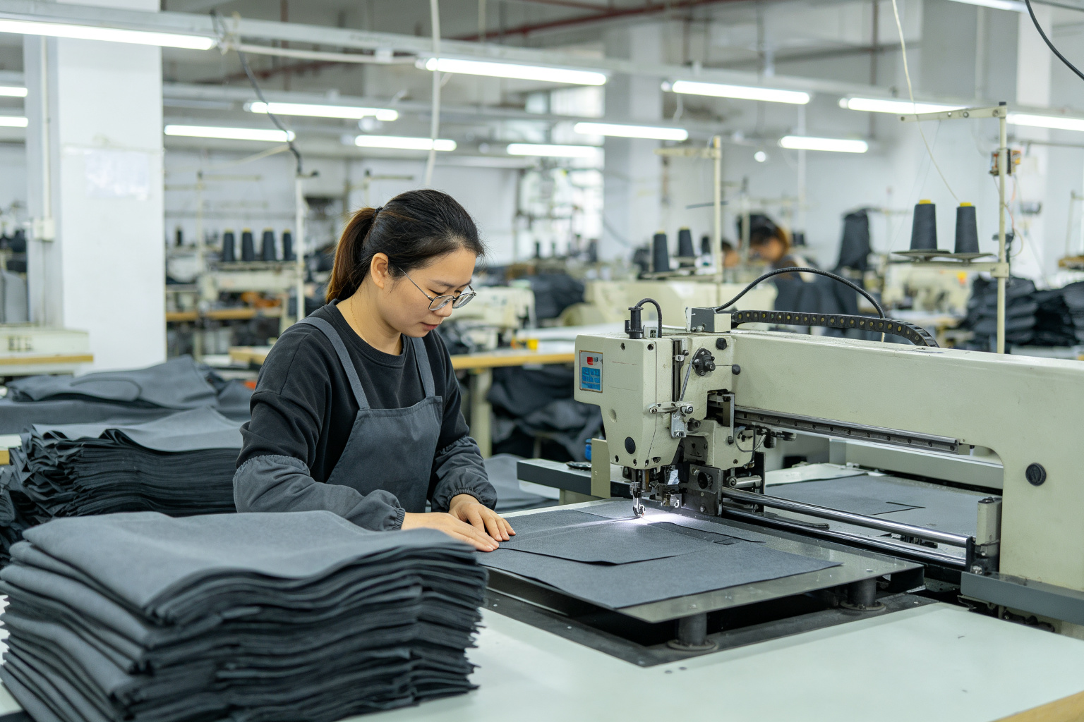 Factory worker cutting charcoal grey RPET fabric panels with a cutting machine in a bag factory