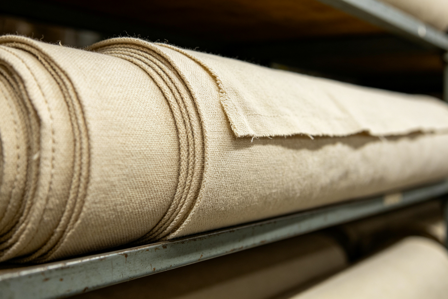 Close-up of a natural 8oz cotton canvas fabric roll showing the woven texture on a factory shelf
