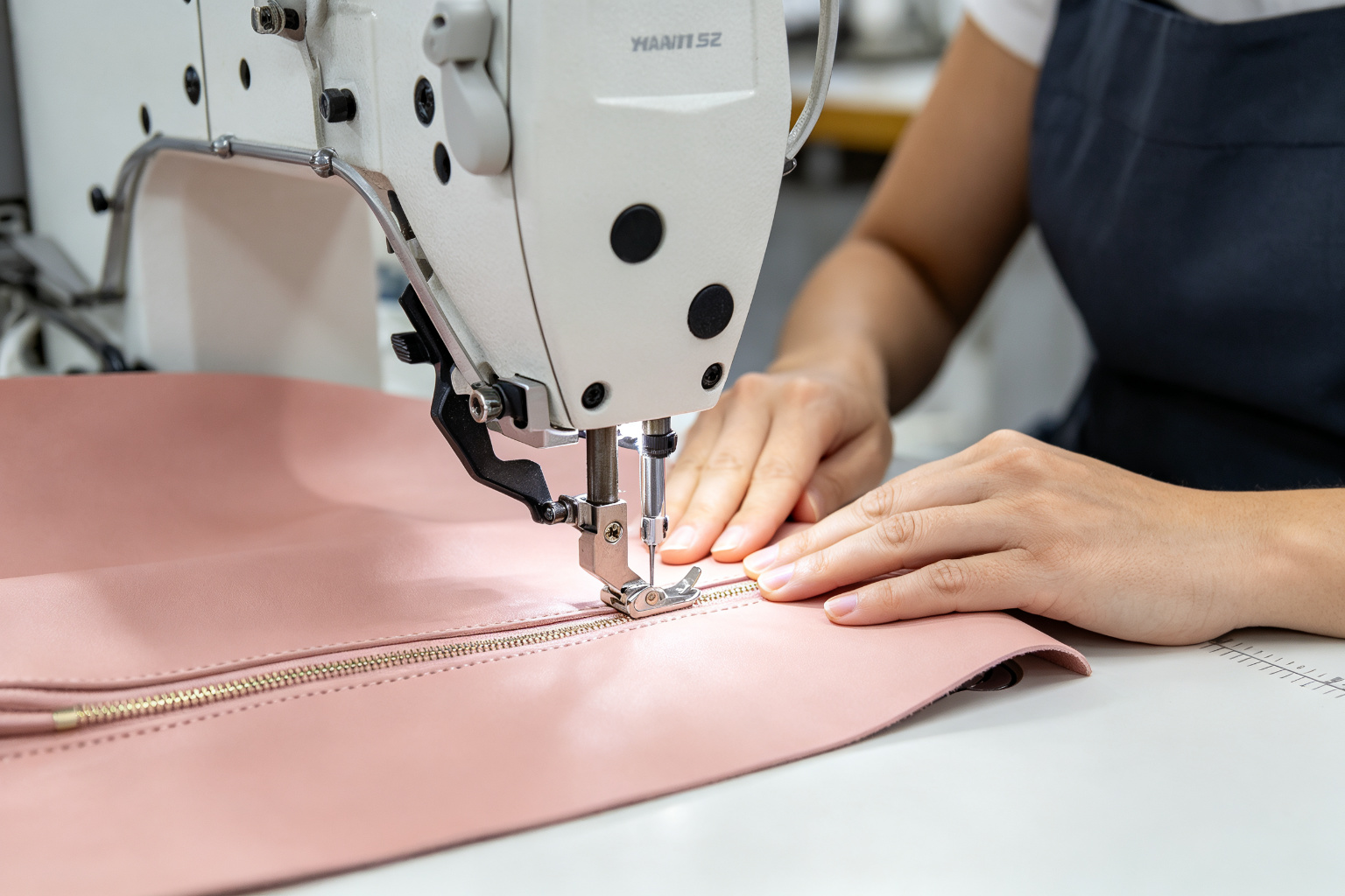 Sewing production line with a worker sewing blush pink PU vegan leather cosmetic case on an industrial sewing machine