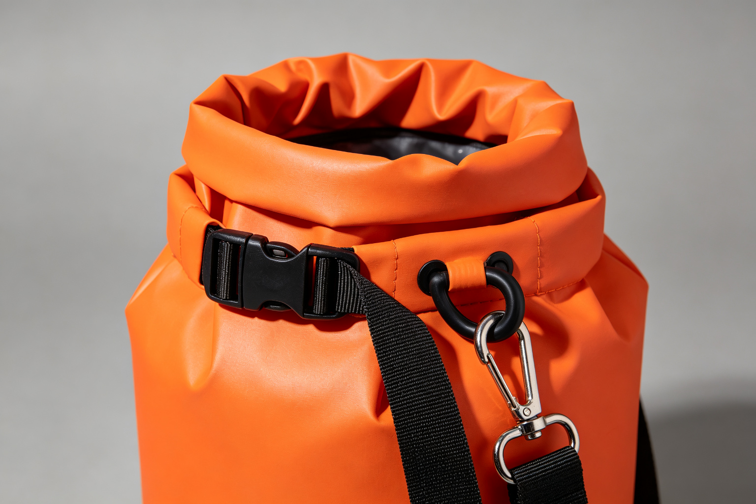 Close-up detail of the roll-top closure on a PVC tarpaulin dry bag showing the triple-roll fold, quick-release side buckle, D-ring, and adjustable shoulder strap with metal swivel hook