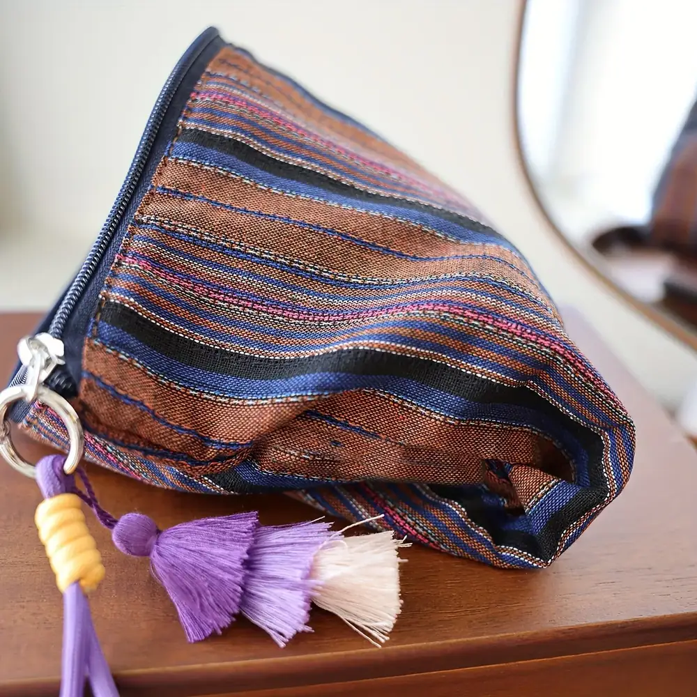 Boho striped fabric cosmetic pouch with woven fringe tassel on a wood surface