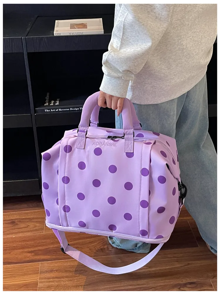 Person holding light purple polka dot duffel bag indoors
