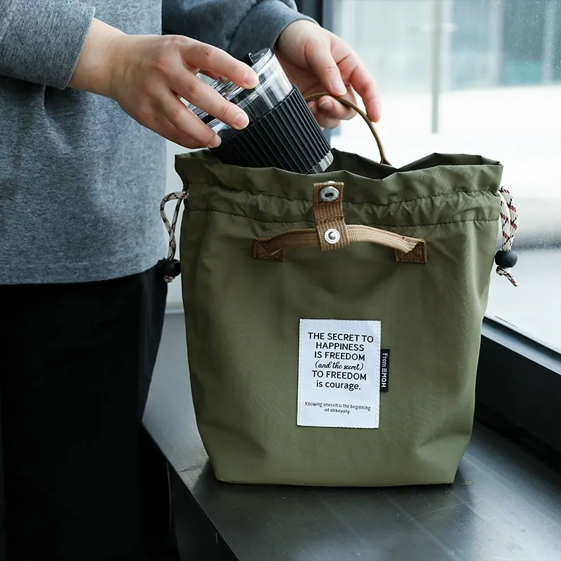 Olive drawstring bento bag holding a travel mug for daily commute