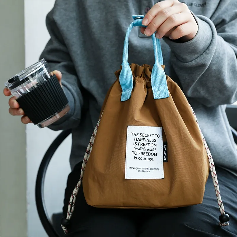 Tan drawstring lunch bag with light blue handle and red-white drawcord