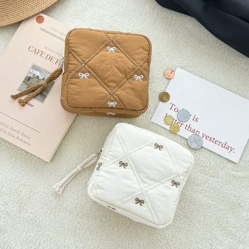 Caramel quilted cosmetic bag with white embroidered bow on a soft surface