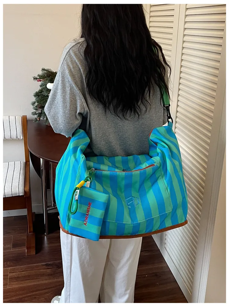 Person carrying striped swim duffel bag over shoulder outdoors