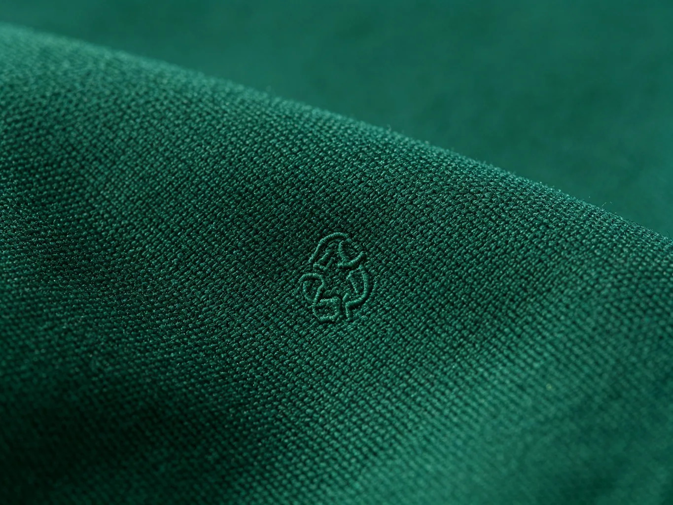 RPET recycled polyester fabric texture close-up, dark green with recycle symbol